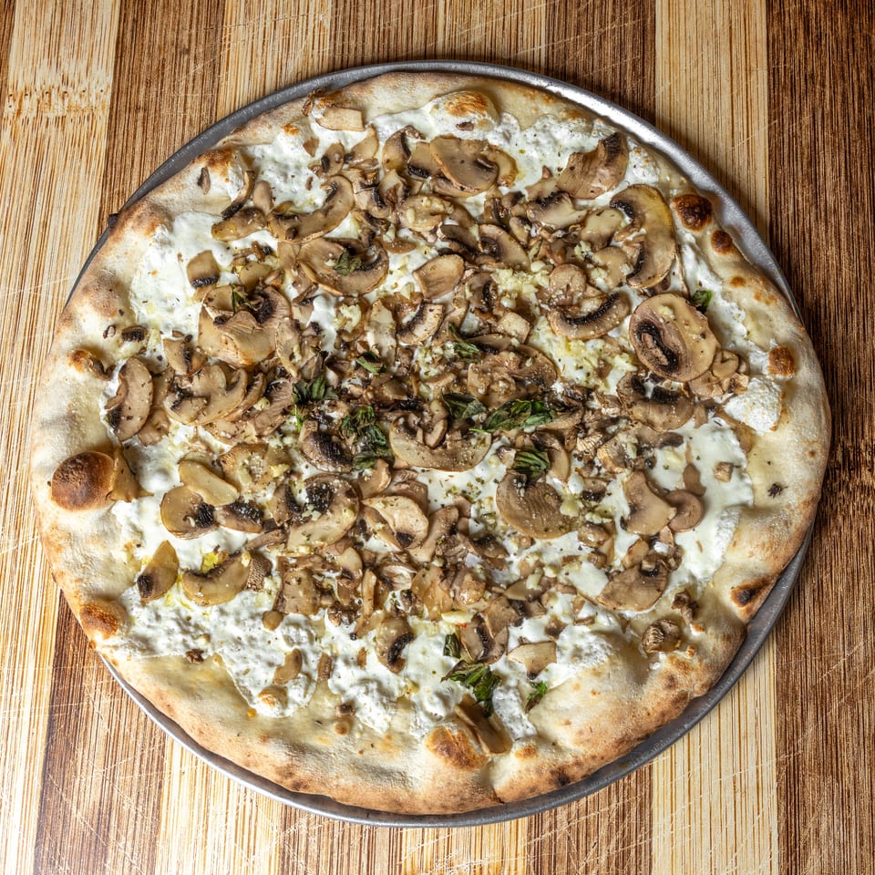 White pizza with mushrooms, ricotta cheese, garlic, and herbs on a wooden table.