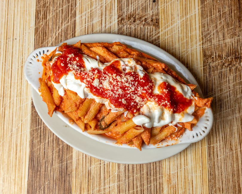 Baked penne pasta with red sauce, melted cheese, and grated parmesan in a white dish.