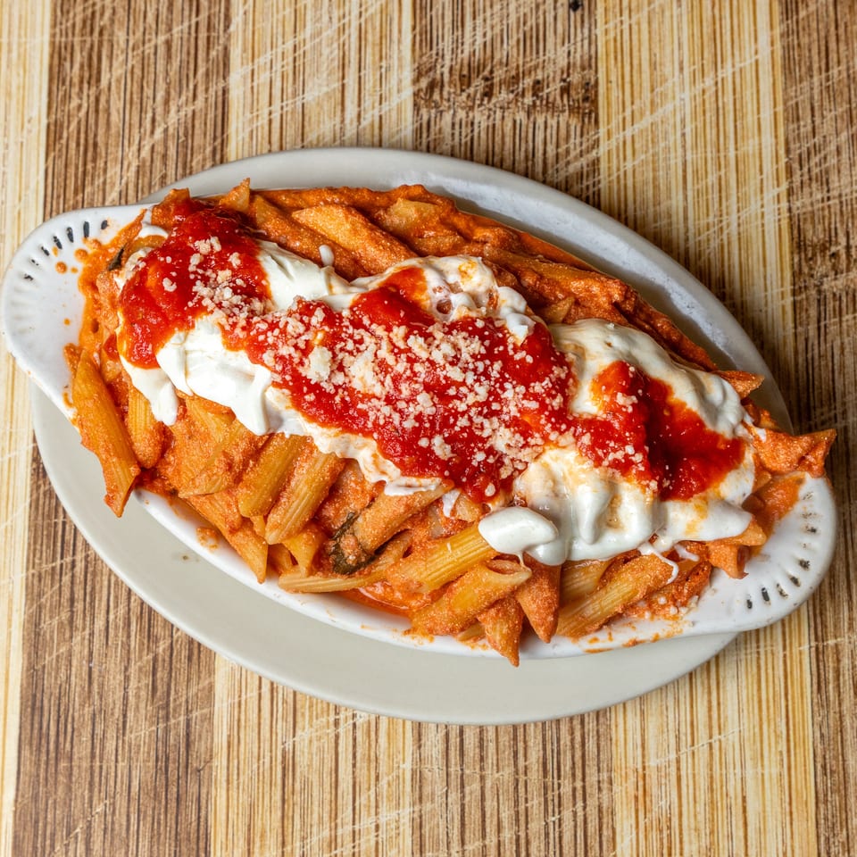 Baked penne pasta with red sauce, melted mozzarella, and grated parmesan cheese in a white dish.